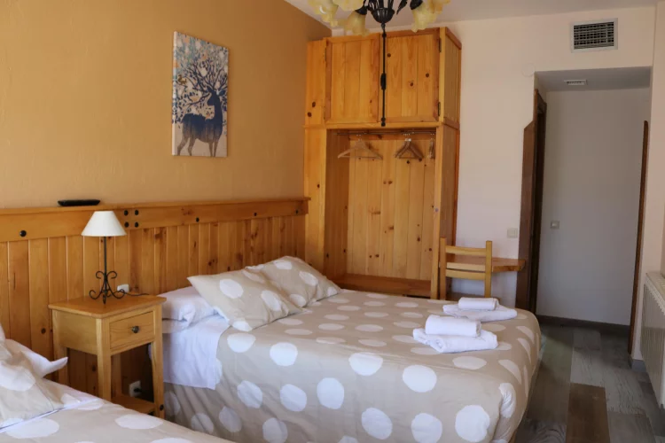 Imagen de Habitación 7. Cuenta con una cama de matrimonio y una cama individual. Tiene baño privado, aire acondicionado, calefacción y televisión. Se encuentra en la primera planta del alojamiento y su ventana da a la calle del alojamiento. Cuenta con un pequeño balcón con unas magníficas vistas. 